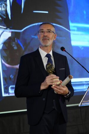 Christophe Baudin sur scène à Lecce recevant une distinction honorifique avec la statuette et le parchemin Ulysse